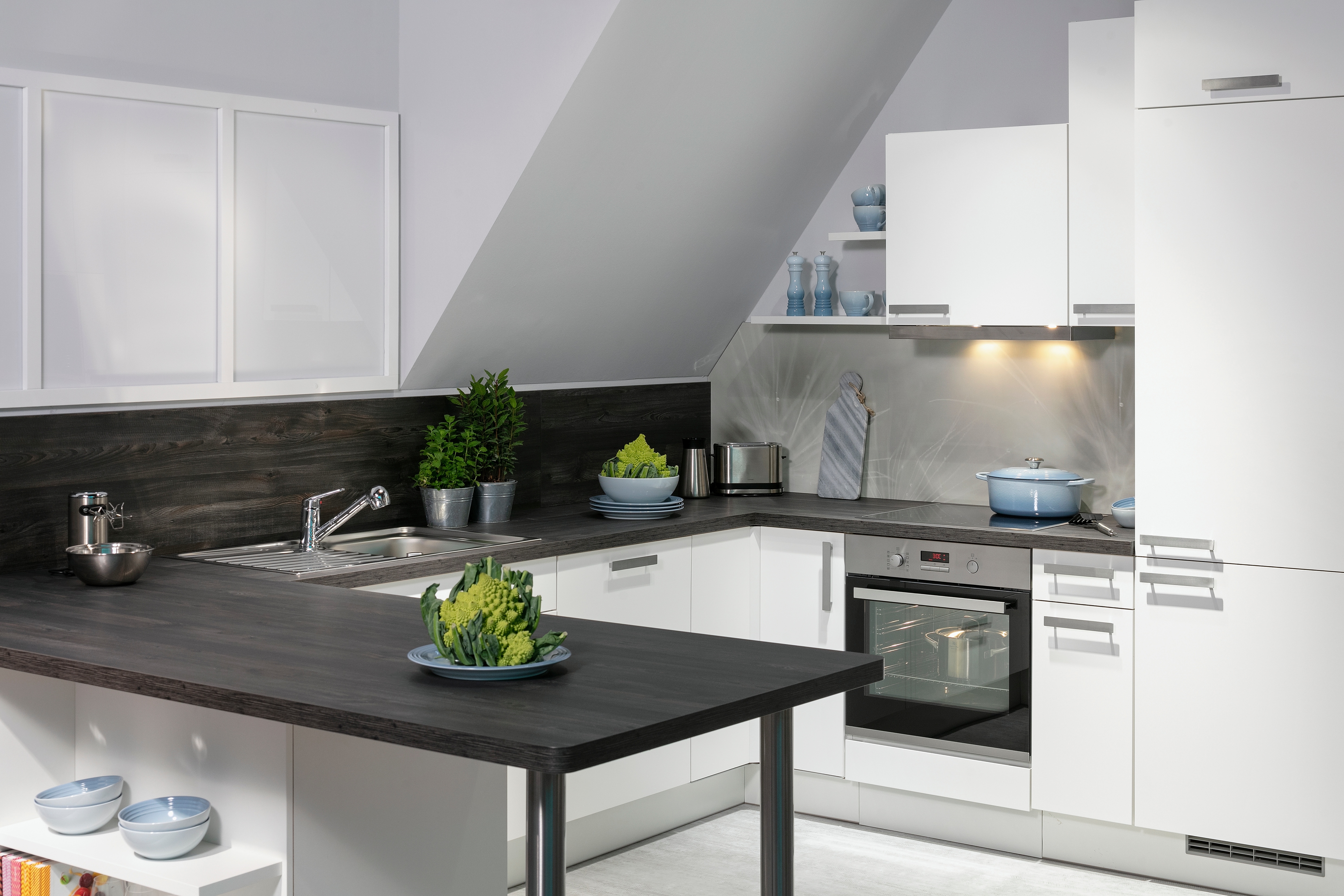 Moderne weiße Küche mit dunkler Arbeitsplatte unter Dachschräge, Pflanzen auf der Theke.