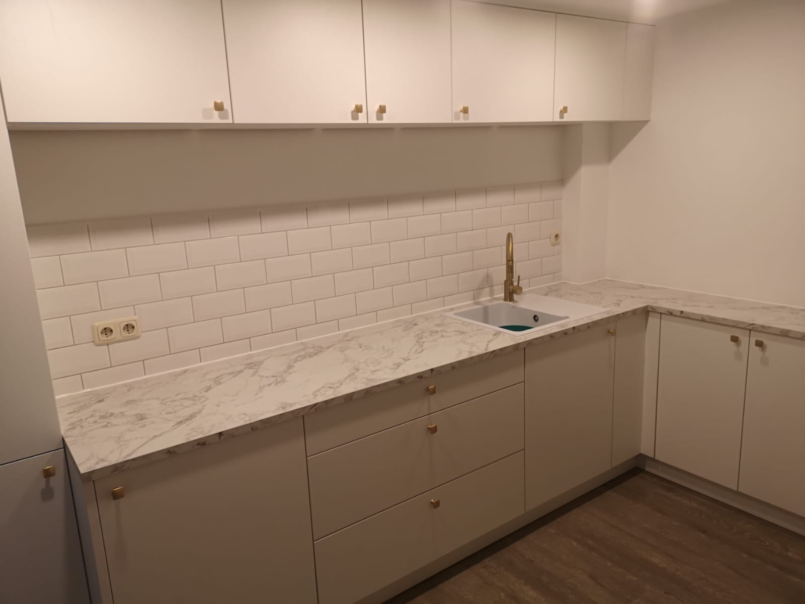 Moderne, weiße Küche mit Marmorarbeitsplatte und goldfarbenem Wasserhahn.