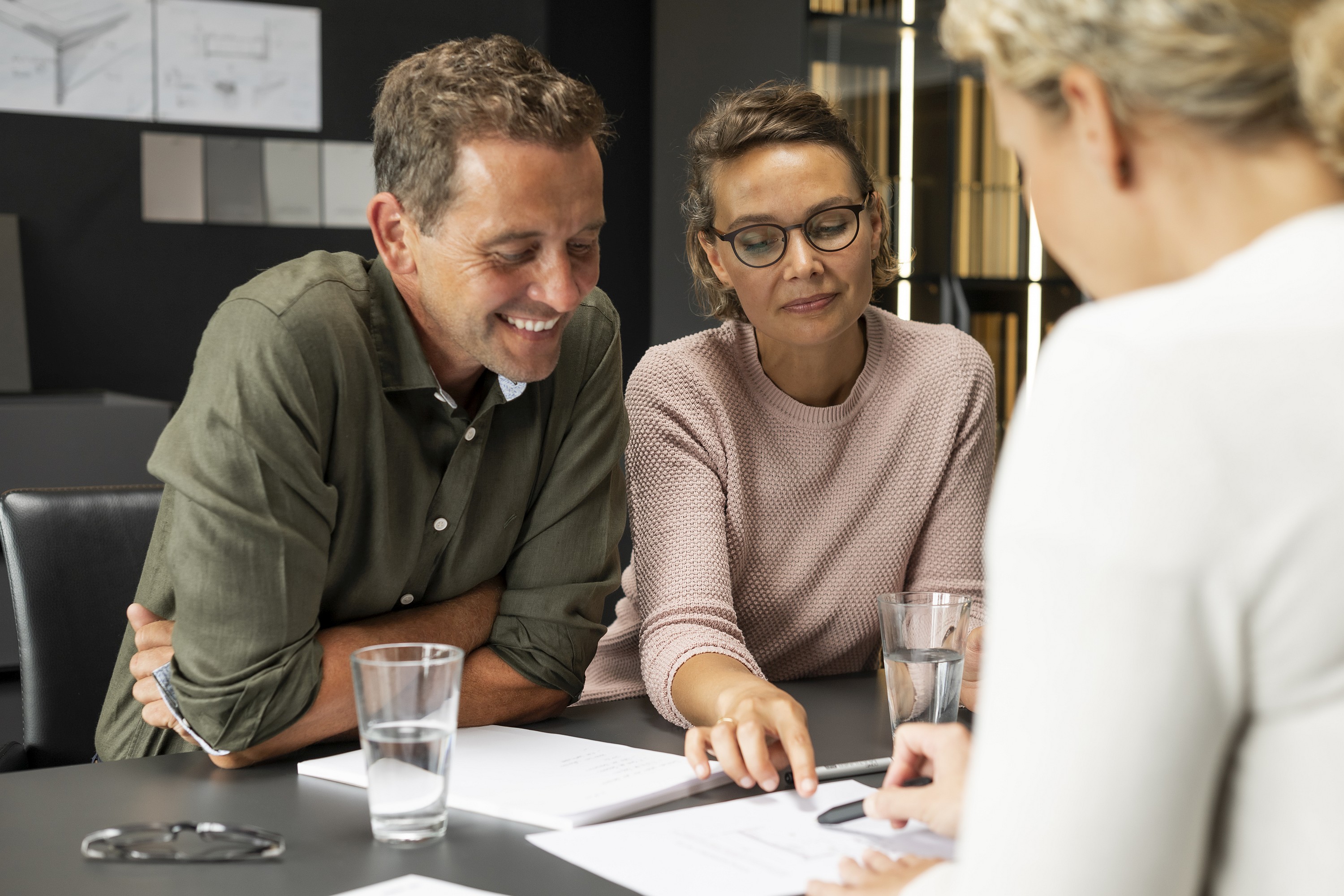 Lachender Mann und neben ihm seine eher kritisch blickende Frau im Küchenstudio bei der Besprechung mit der Küchenplanerin