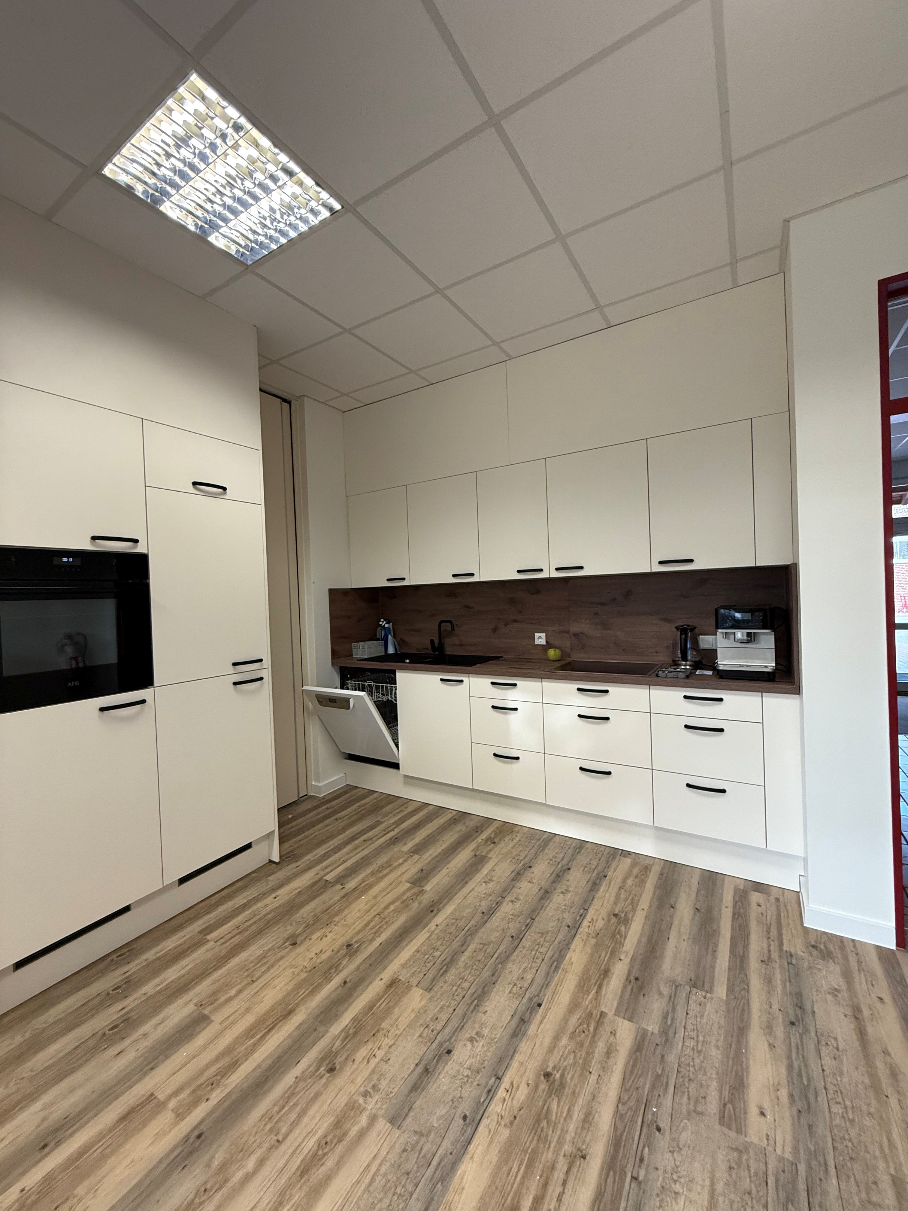 Moderne, helle Büroküche mit weißen Schränken und Holzfußboden.