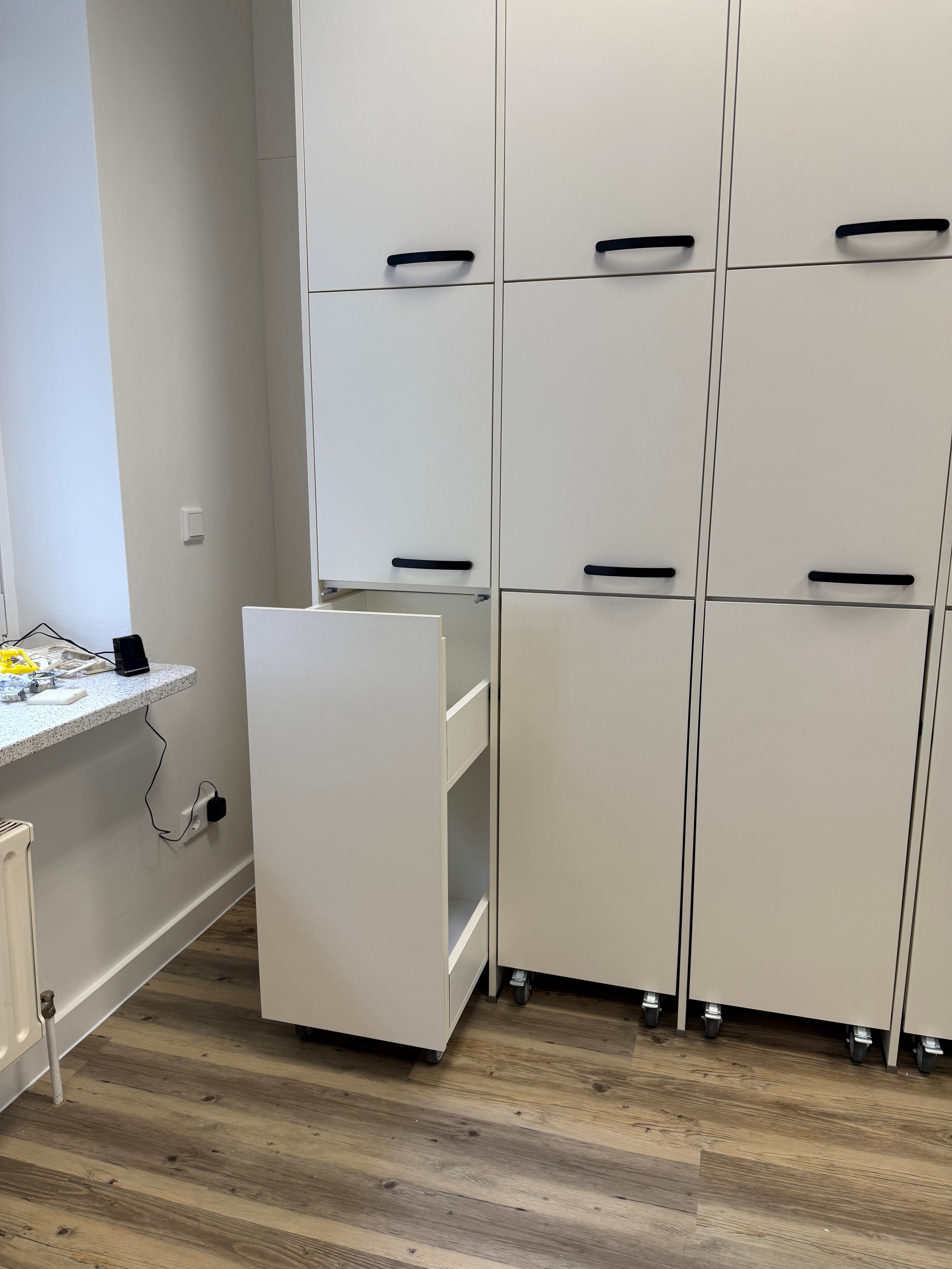 Weißer Schrank mit herausgezogenem Schubladenelement, Holzboden, helle Wand.