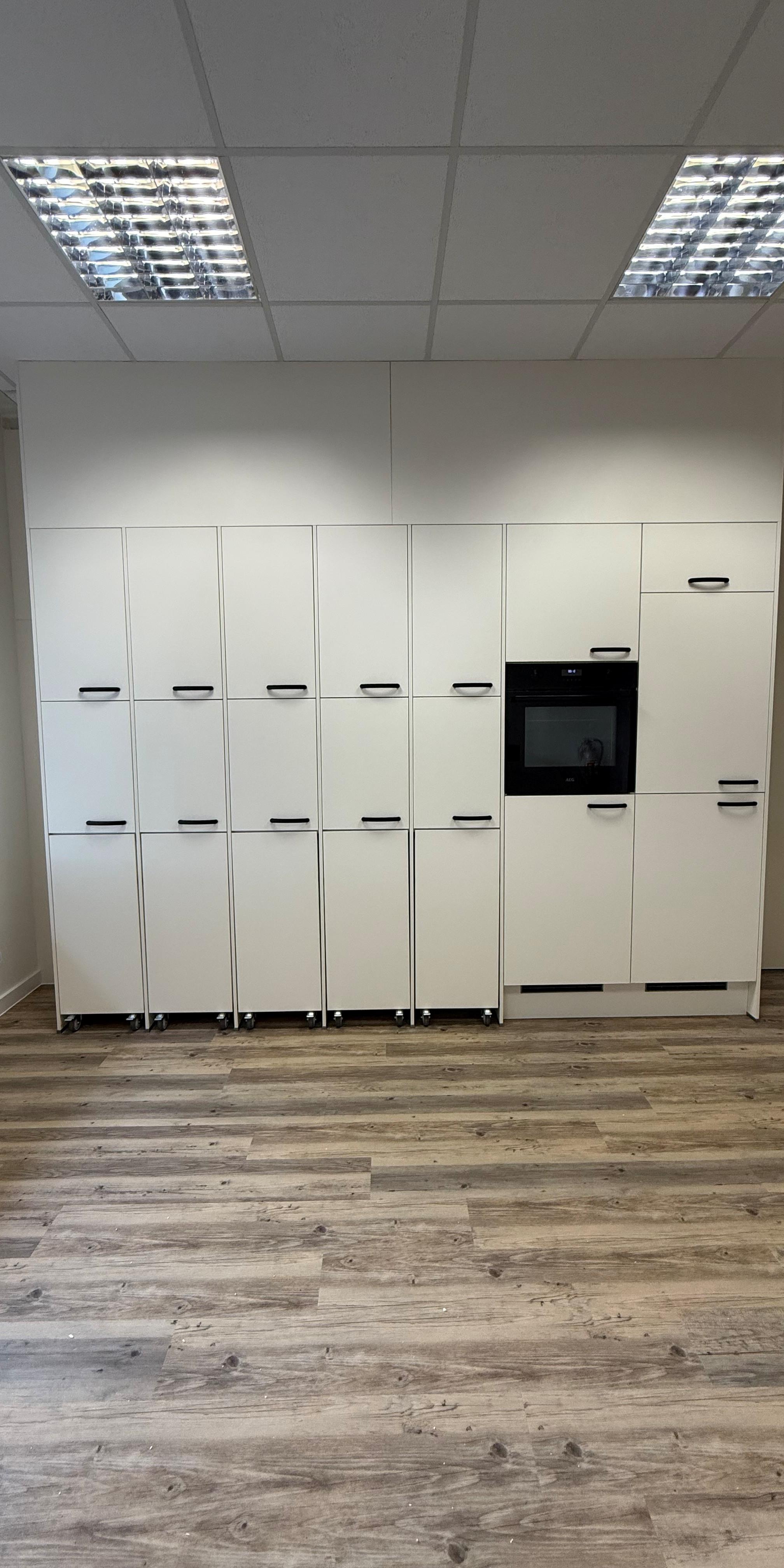 Moderne Küche mit weißen Schränken, Einbaubackofen und Holzfußboden.